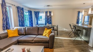 Ein modernes Wohnzimmer mit einem braunen Ecksofa, einem weißen Couchtisch und einem Essbereich mit einem kleinen Tisch und Stühlen.