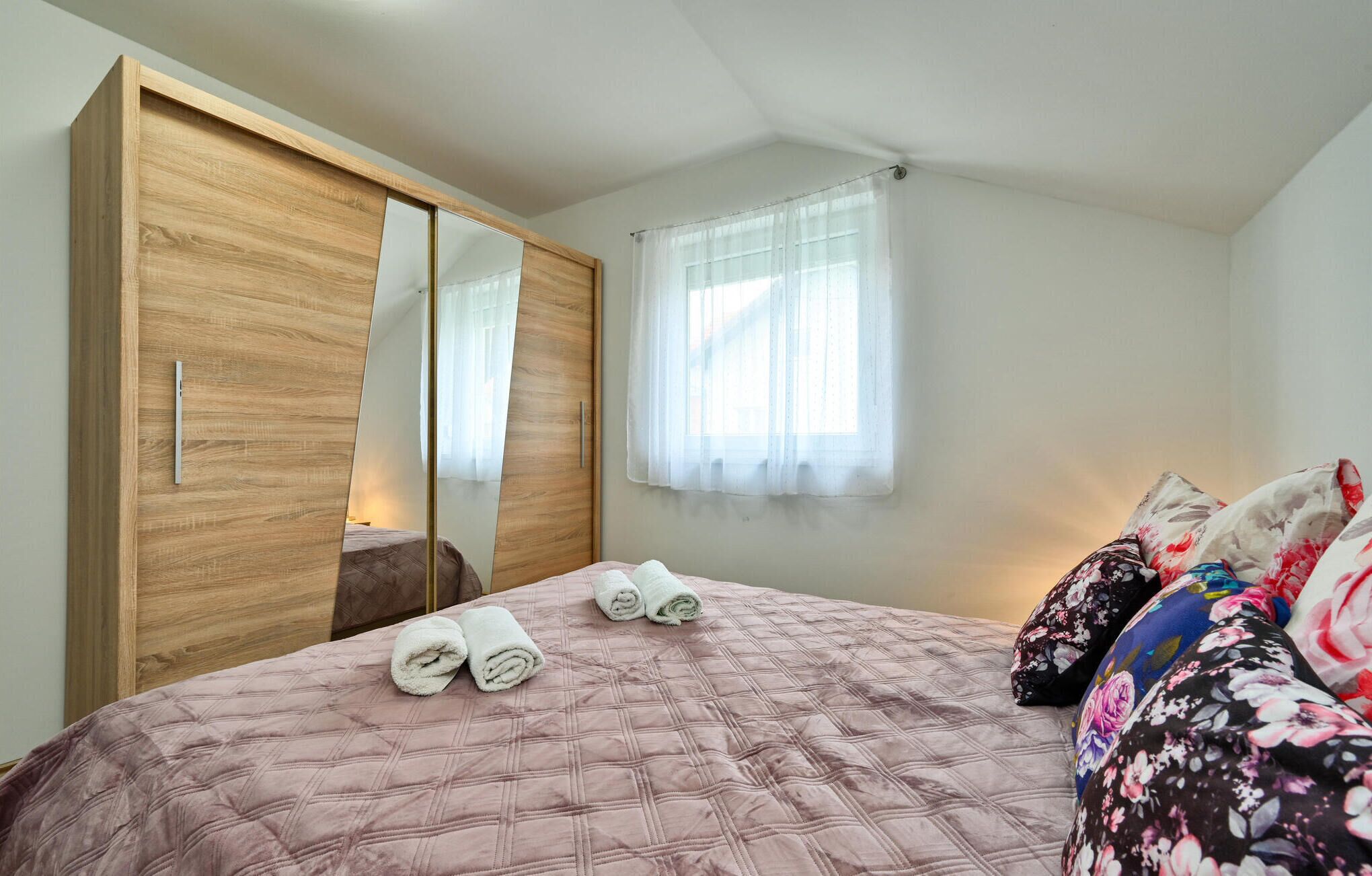 Een slaapkamer met een bed, een kledingkast, een spiegel en een raam met gordijnen.