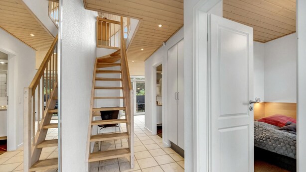 A modern interior with a wooden staircase, white walls, and a visible kitchen area. - Beautiful home in Nørre Nebel (Nørre Nebel)
