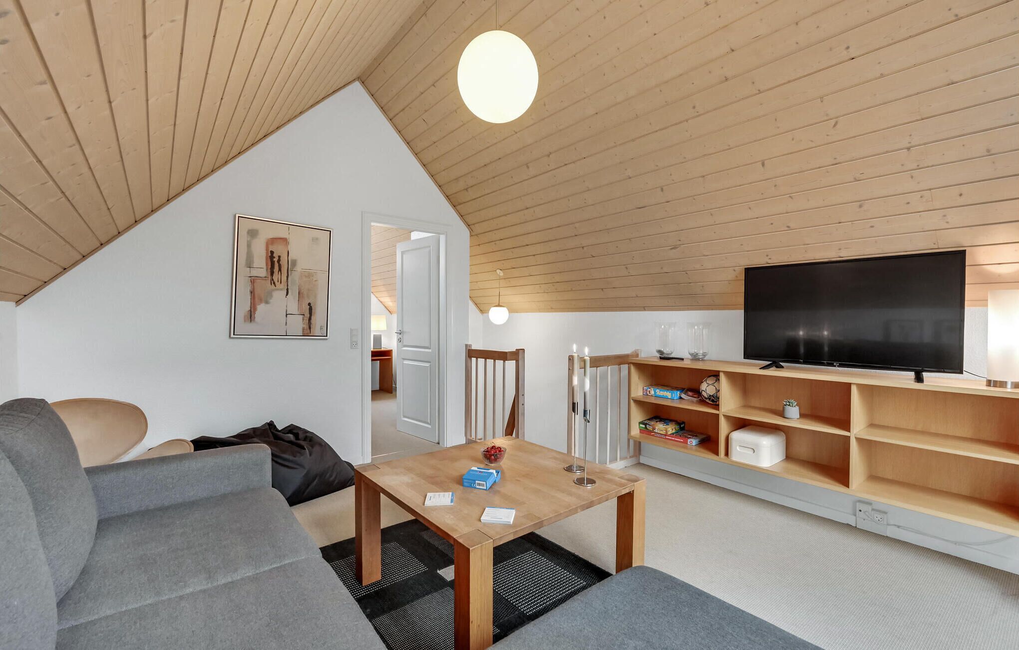 A modern living room with a sloped ceiling, a flat-screen TV, a wooden coffee table, and a grey sofa.