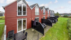 A row of red wooden houses with white trim, each featuring a balcony and a patio area with outdoor furniture. - Beautiful home in Nørre Nebel (Nørre Nebel)