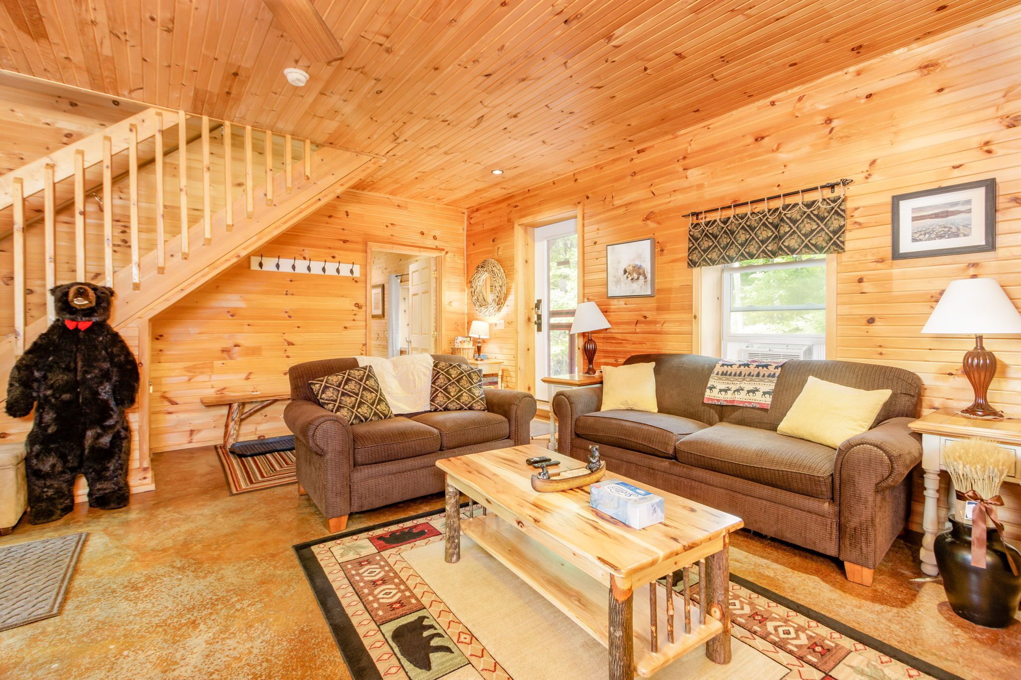 L’intérieur d’un chalet en bois, avec un escalier, deux canapés, une table basse et une statue d’ours.