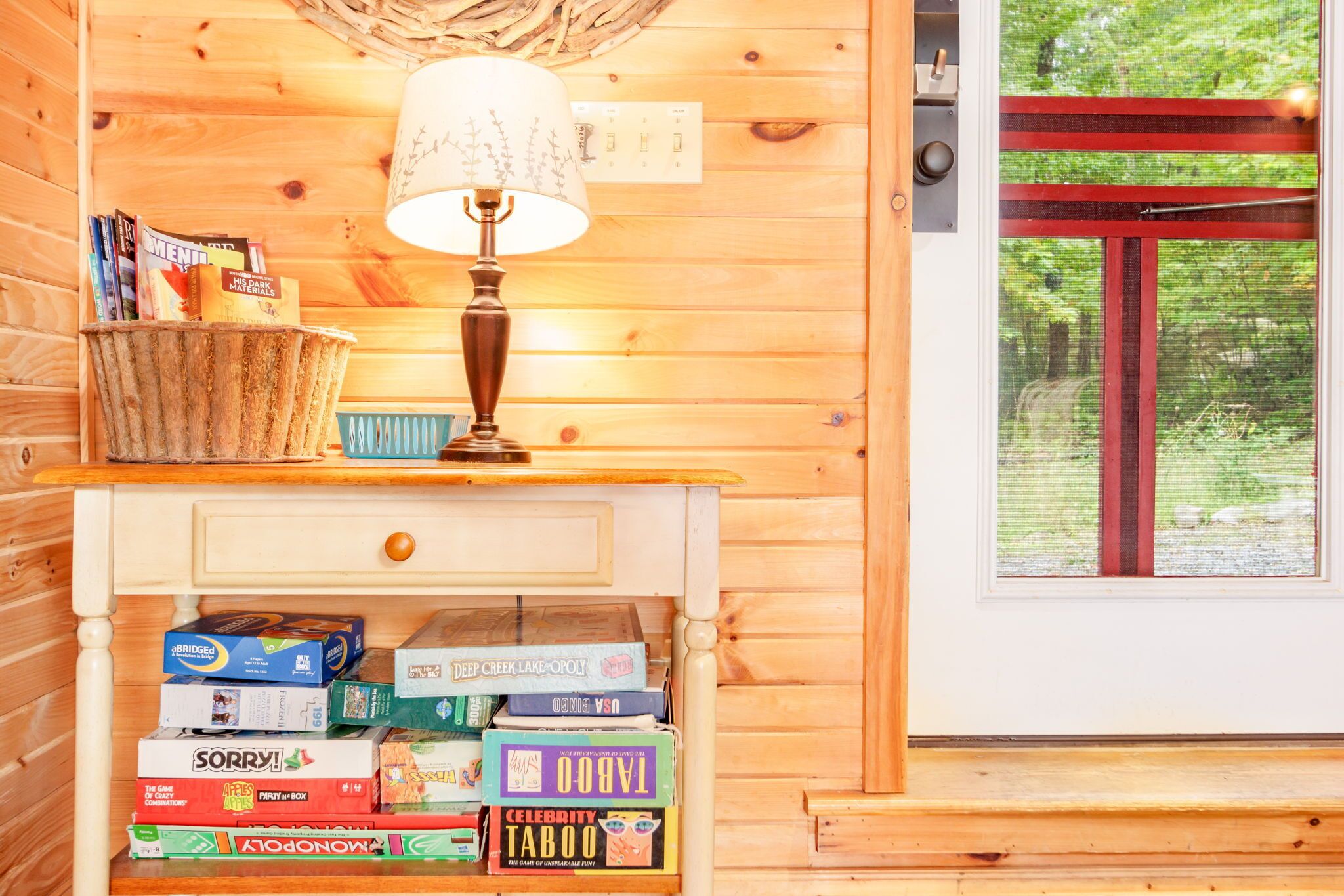 Un interior de madera con una lámpara, una cesta de libros y una estantería con juegos de mesa.