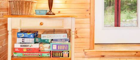 Un interior de madera con una lámpara, una cesta de libros y una estantería con juegos de mesa.