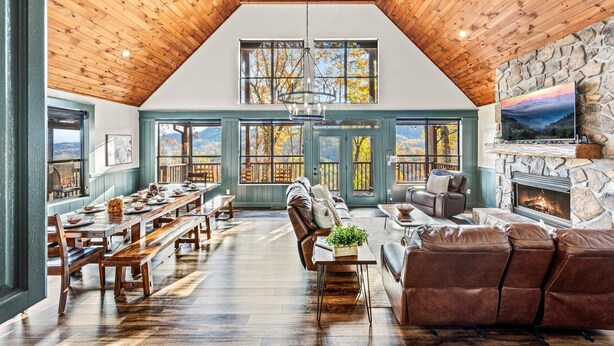 Un loft espacioso con techo alto, vigas de madera, chimenea de piedra y ventanas amplias que ofrecen vistas al exterior.