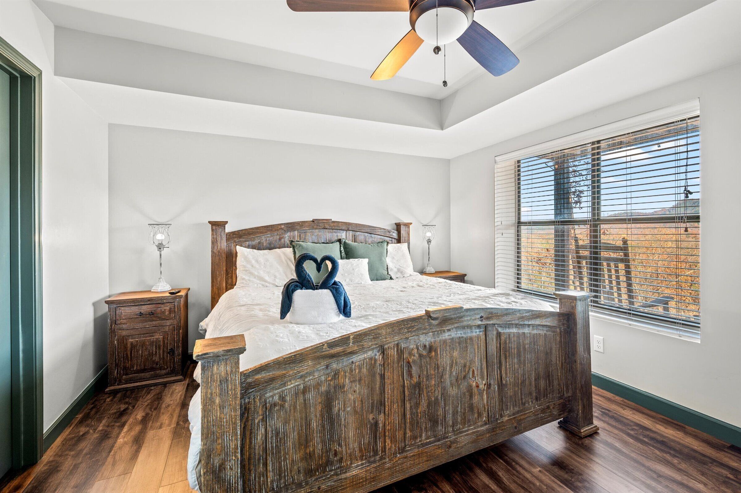 A bedroom with a wooden bed, white walls, a ceiling fan, and a window with blinds.