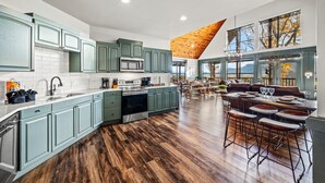 Una cocina amplia con armarios color turquesa, una isla central y un comedor con techo de madera y ventanas grandes.