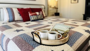 A neatly made bed with a quilt, pillows, and a tray with coffee mugs and a magazine.