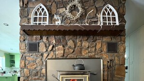A stone fireplace with a modern wood-burning stove, decorative elements above, and a metal fireguard.