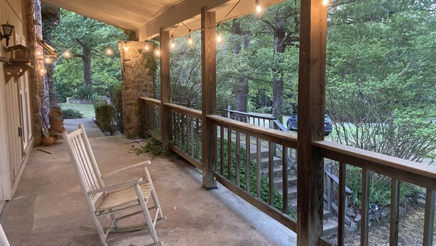 A wooden porch with a rocking chair, string lights, and a view of a forested area.