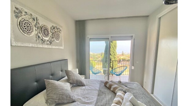 Ein Schlafzimmer mit einem großen Bett, einer Kopfteil und Blick ins Freie durch eine Schiebetür.