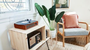 A wooden cabinet with a vintage radio, a potted plant, and a chair with a cushion.