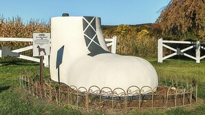 A large, white, sculptural installation resembling a dog house with a sign indicating it is for sale.