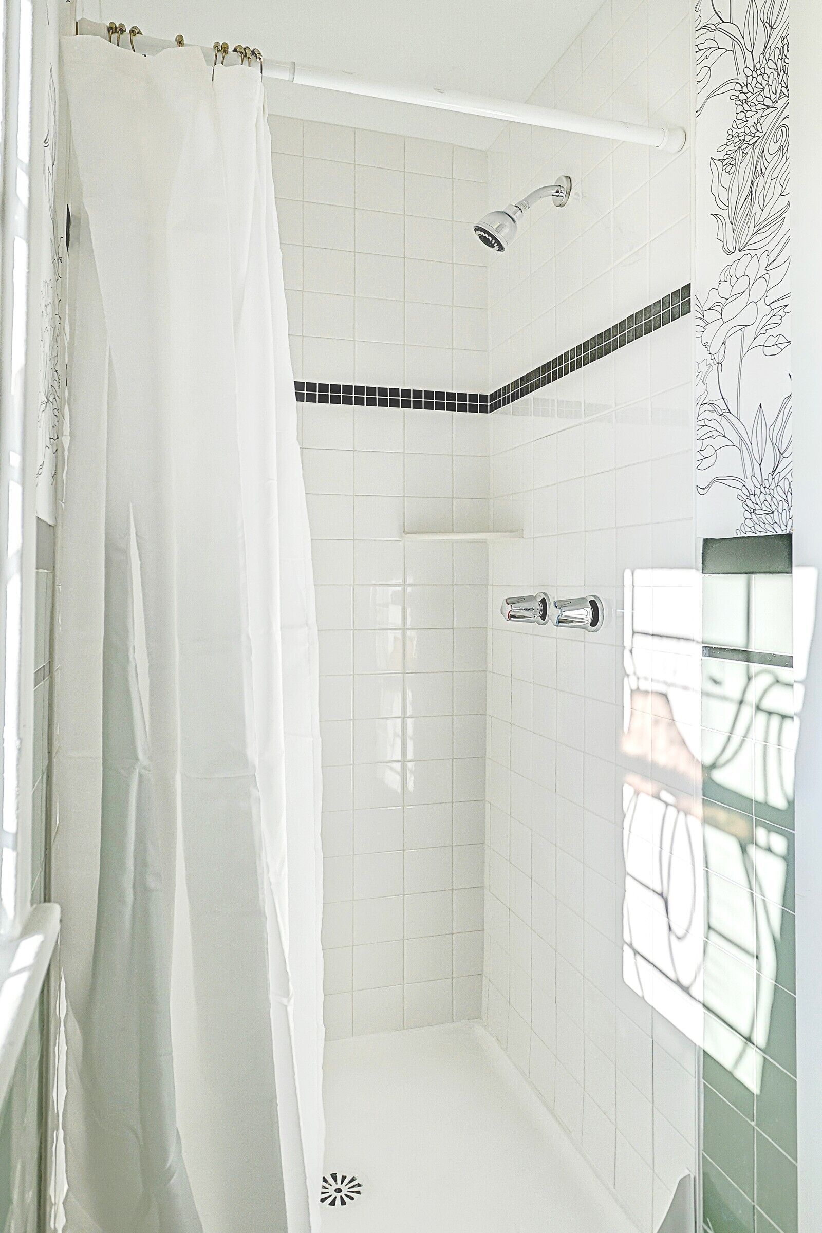Ducha con cortina blanca, cabezal de ducha de mano y pared de azulejos con diseño blanco y negro.