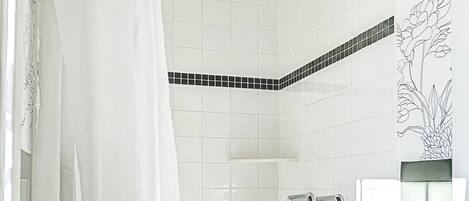Ducha con cortina blanca, cabezal de ducha de mano y pared de azulejos con diseño blanco y negro.