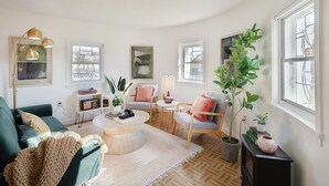 A cozy living room with a green sofa, a round coffee table, and a fireplace. There are several windows providing natural light and a view of the outside.