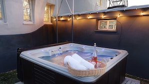 A hot tub with two white towels and a bottle, surrounded by a dark wall and string lights.