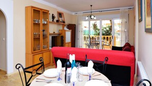 Un coin repas avec un canapé rouge, un buffet en bois doté de portes en verre et une table à manger dressée pour quatre personnes.