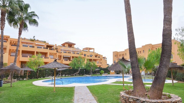 Une piscine entourée de palmiers et un bâtiment doté de balcons.