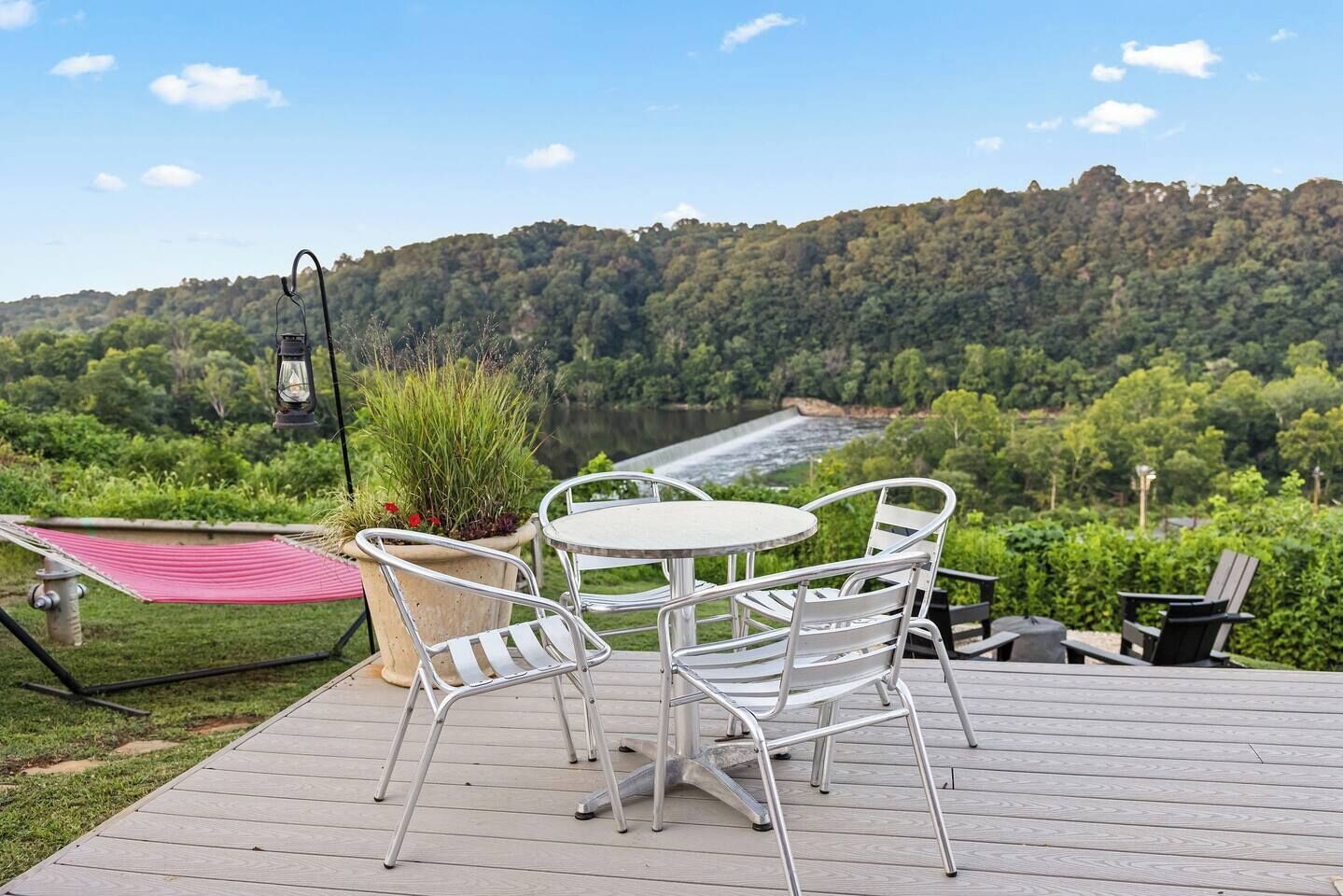 A deck with a table and chairs, overlooking a river and forested hills.