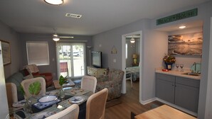 A well-lit living room with a dining area, a kitchen, and a bedroom.