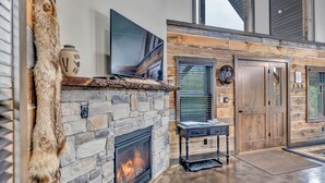 A stone fireplace with a TV above it, a wooden door, and a fur throw on the wall. - Rustic Hideaway Sleeps 4 HOT TUB (De Soto)