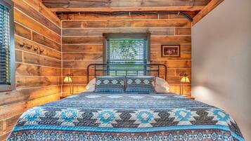 A wooden cabin room with a bed, two wall-mounted lamps, and a window with blinds.
