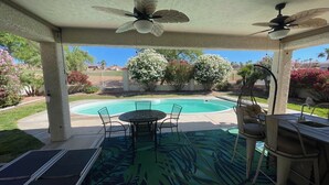 Un patio couvert avec une piscine, du mobilier d’extérieur et des ventilateurs de plafond.