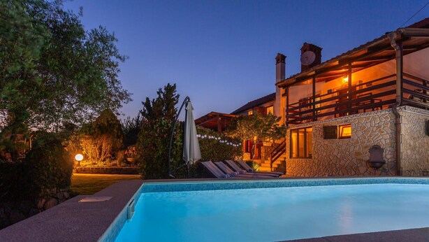 Une piscine avec un mur en pierre et une terrasse en bois. On y trouve également un bâtiment doté d’un balcon et d’une antenne parabolique.