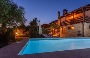 A swimming pool with a stone wall and a wooden deck. There is a building with a balcony and a satellite dish. - Awesome home in Risika (Risika)