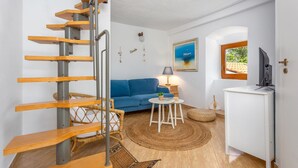 Un salon moderne avec un escalier en colimaçon, un canapé bleu, une petite table ronde et un meuble blanc.