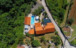 An aerial view of a property with a swimming pool, multiple buildings with red roofs, and surrounding greenery. - Awesome home in Risika (Risika)