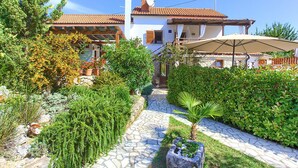 Une villa avec un toit en tuiles, un chemin de pierre et une végétation luxuriante.
