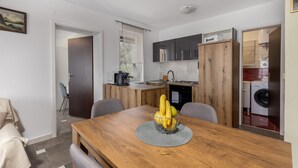 Eine kompakte Küche mit modernen Geräten, ein Essbereich mit Holztisch und -stühlen sowie ein sichtbarer Waschbereich.