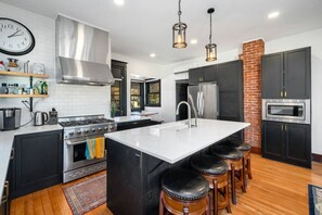 A modern kitchen with a central island, stainless steel appliances, and black cabinetry. - Mountain Manor in Sandy| HotTub |3KingBeds| MtHood (Sandy)