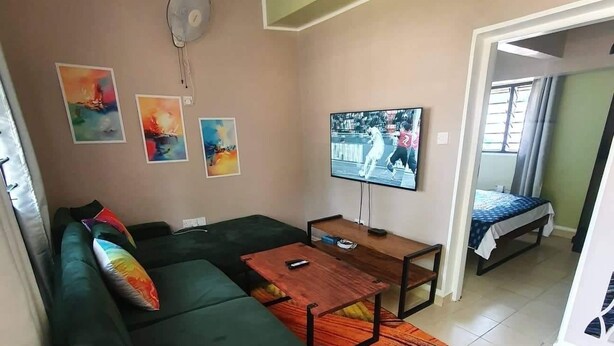 A living room with a green sofa, a wooden coffee table, a TV, and abstract wall art. - Beach-side one bedroom (Kwale County)