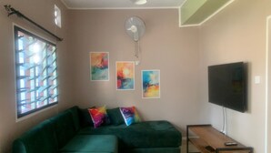A living room with a green sectional sofa, a flat-screen TV, and abstract art on the wall. - Beach-side one bedroom (Kwale County)