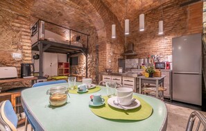 A rustic kitchen with exposed brick walls, a round table with green placemats, and modern appliances. - 1 bedroom beautiful apartment in Roma (Roma)