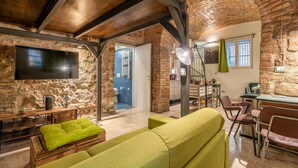 Un interior rústico con paredes de ladrillo visto, un banco de madera con cojín verde, un sofá y una zona de comedor con mesa y sillas.