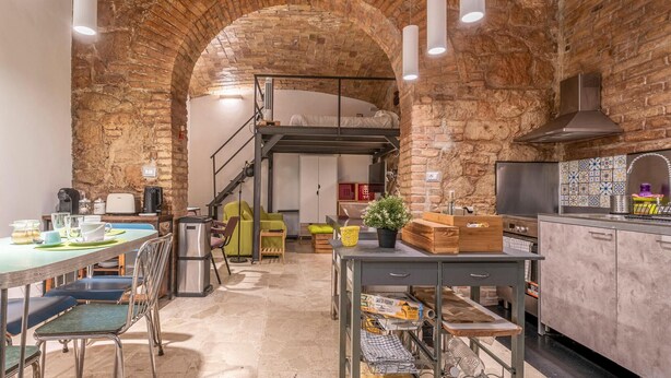 Una cocina amplia con un alto techo de ladrillo en arco, iluminación moderna y una isla central con asientos.