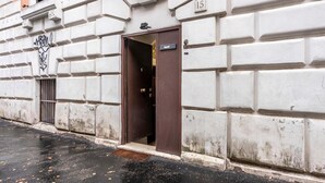 Un edificio con fachada blanca, puerta marrón y una ventana pequeña protegida por una reja de metal.