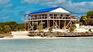 Een twee verdiepingen tellend strandhuis met een blauw dak, houten constructie en meerdere balkons.