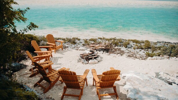 Een strand met houten stoelen en een vuurkuil.