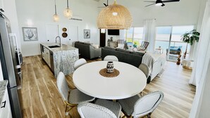 Een ruime woonruimte met een ronde eettafel, rieten stoelen en een grote geweven hanglamp.