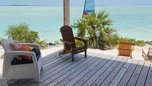 Een houten terras met lounge fauteuils en een zeilboot op de achtergrond.