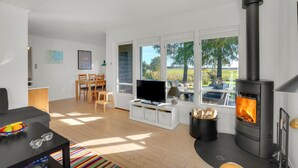 Uma sala de estar moderna com televisão, mesa de jantar, cadeiras, lareira e janelas amplas com vista para o exterior.