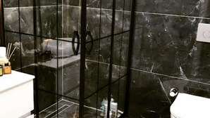 Um banheiro com chuveiro em box de vidro, pia branca e vaso sanitário.