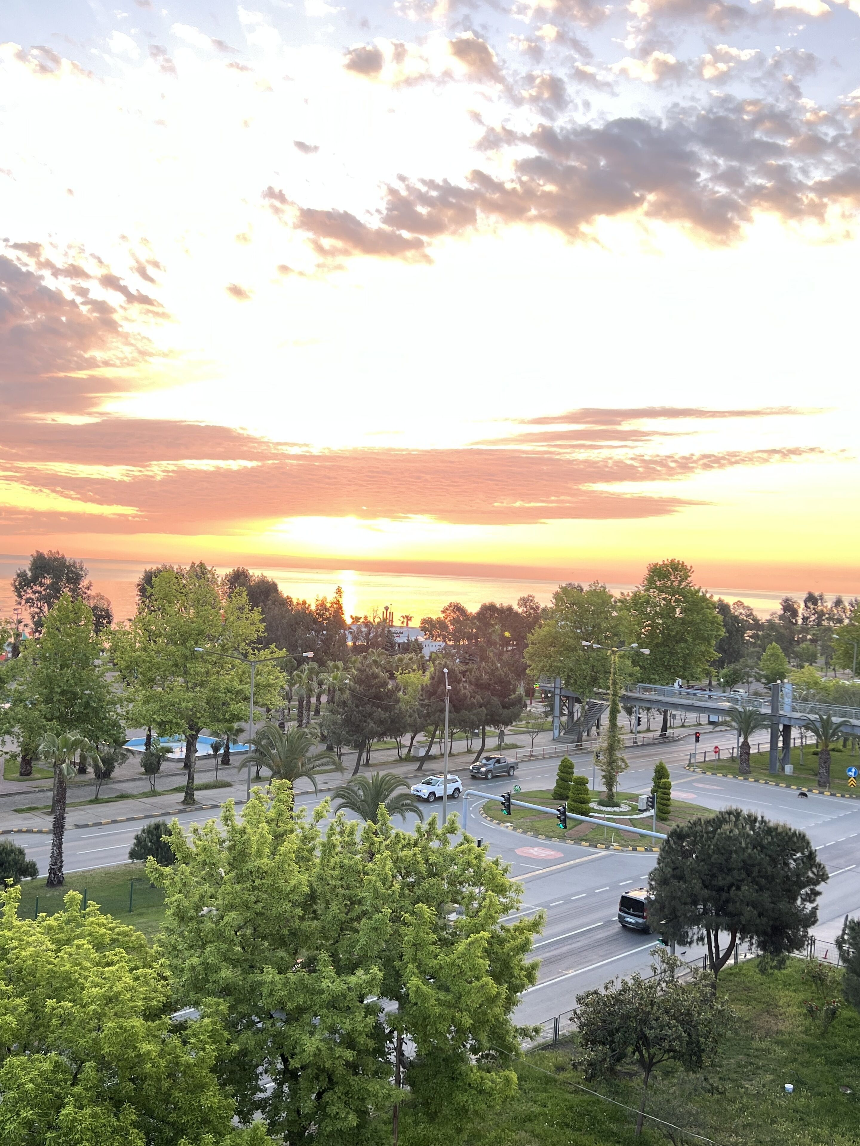 A sunset view over a cityscape with roads, trees, and a bridge.