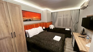 Quarto de hotel com duas camas, uma escrivaninha, televisão e uma janela grande com cortinas.
