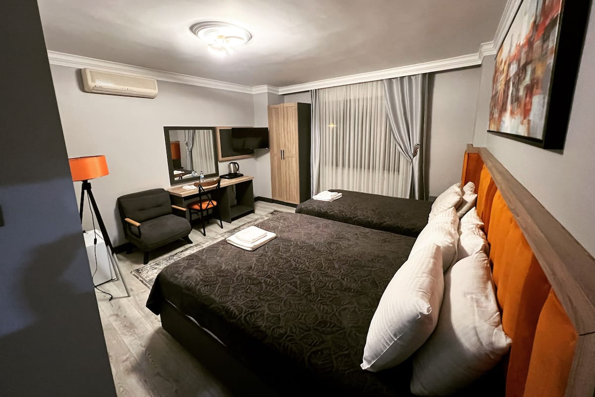 Une chambre d’hôtel avec deux lits, un bureau avec une chaise, une télévision et une fenêtre avec des rideaux.